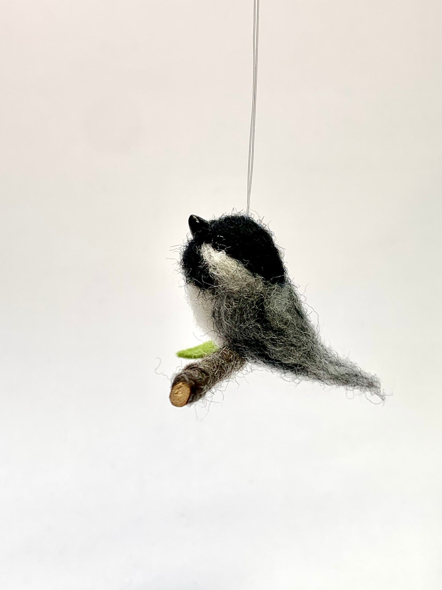 Plush toy resembling a bird on a branch against a white background