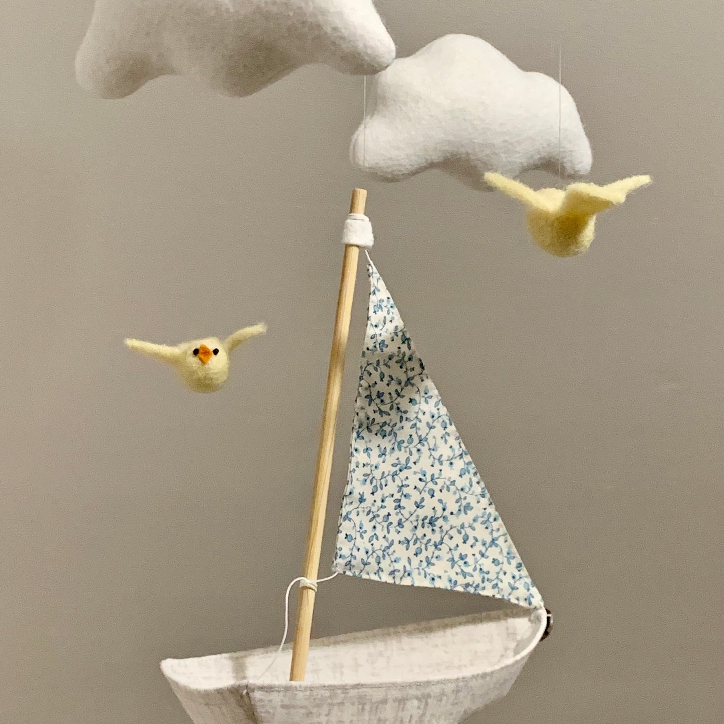 Decorative mobile with clouds, sailboat, and birds against a beige background