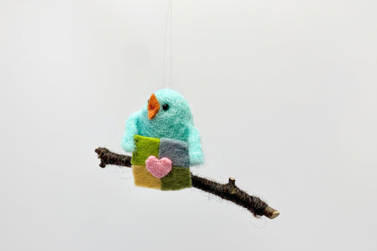 Felted bird ornament with a heart on a branch against a white background