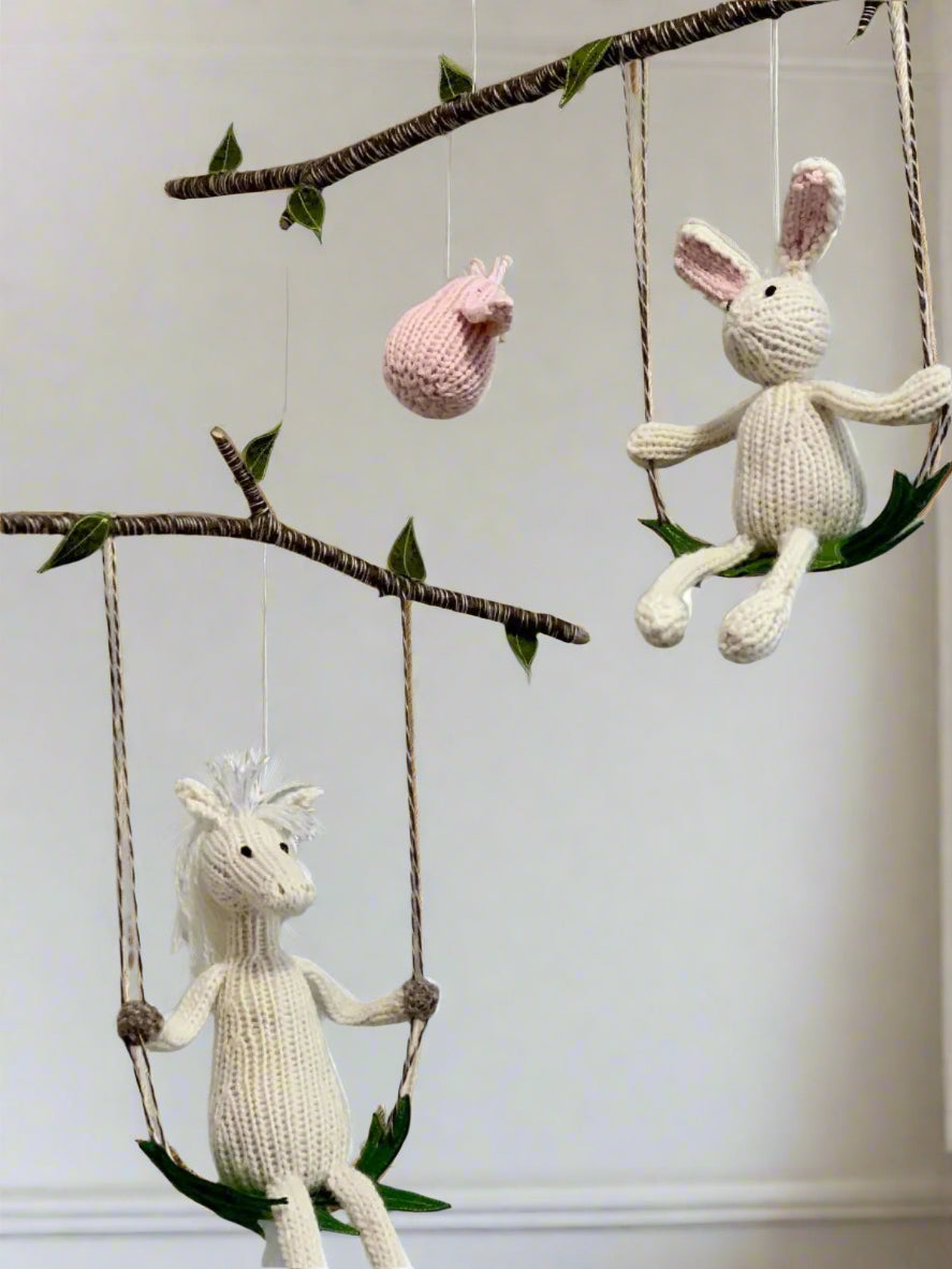 Knitted animal toys hanging from branches against a plain background.