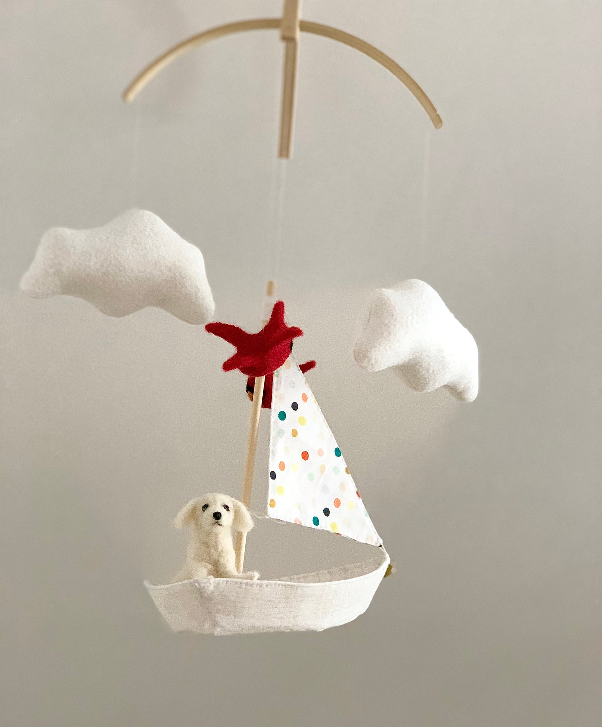 baby mobile of a white needle-felted wool dog sitting in a sailboat with a polk-dot sail and red cardinal birds flying around