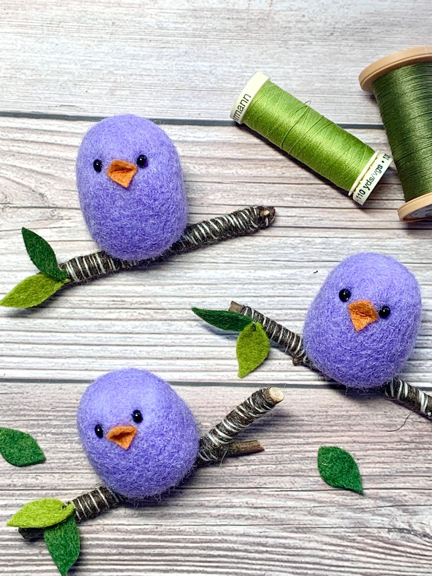 Three handcrafted ornaments of needle-felted two-inch roundish purple birds perched on individual 3-inch branches. 