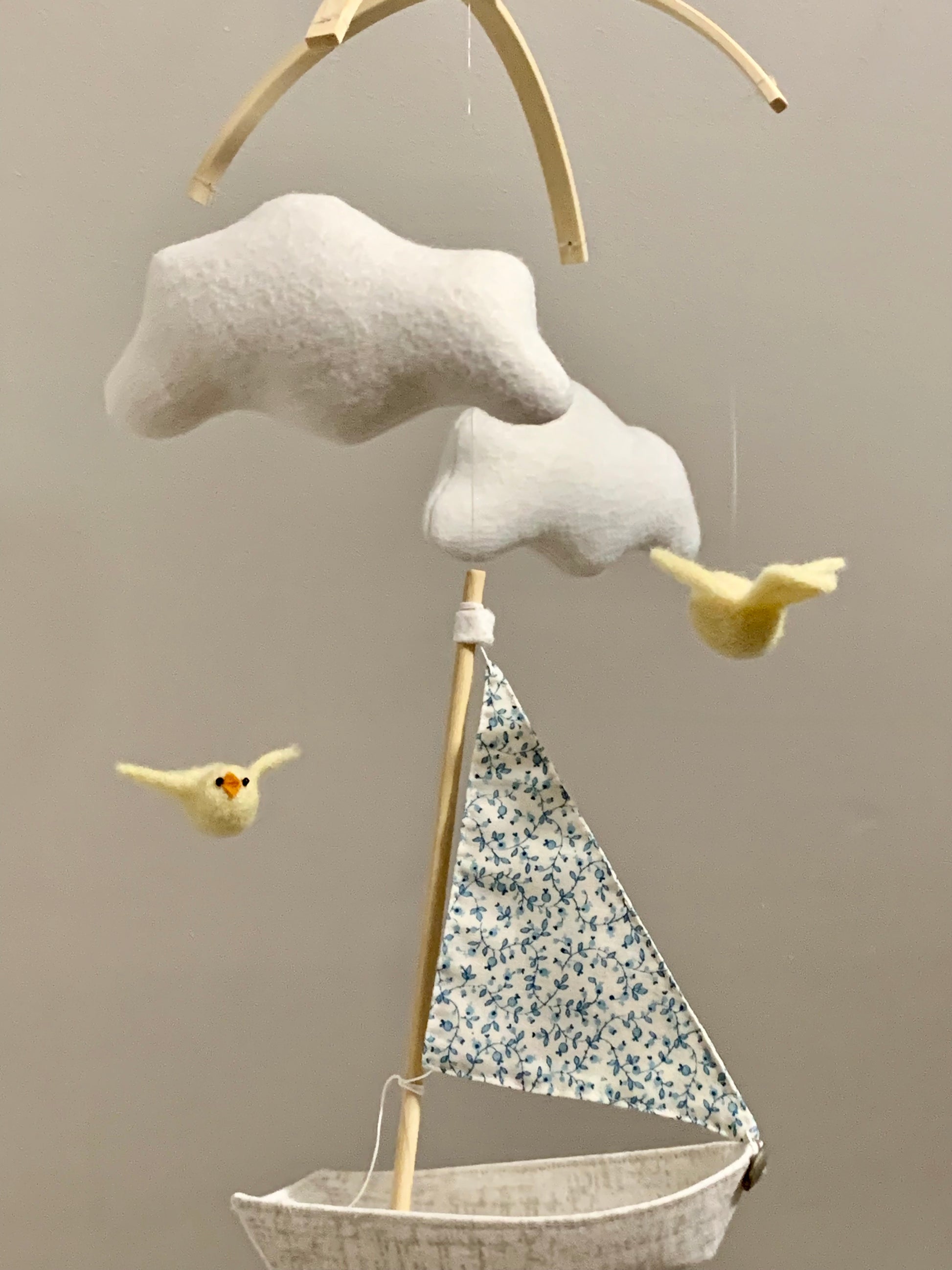 Decorative mobile with cloud, sailboat, and birds against a beige background