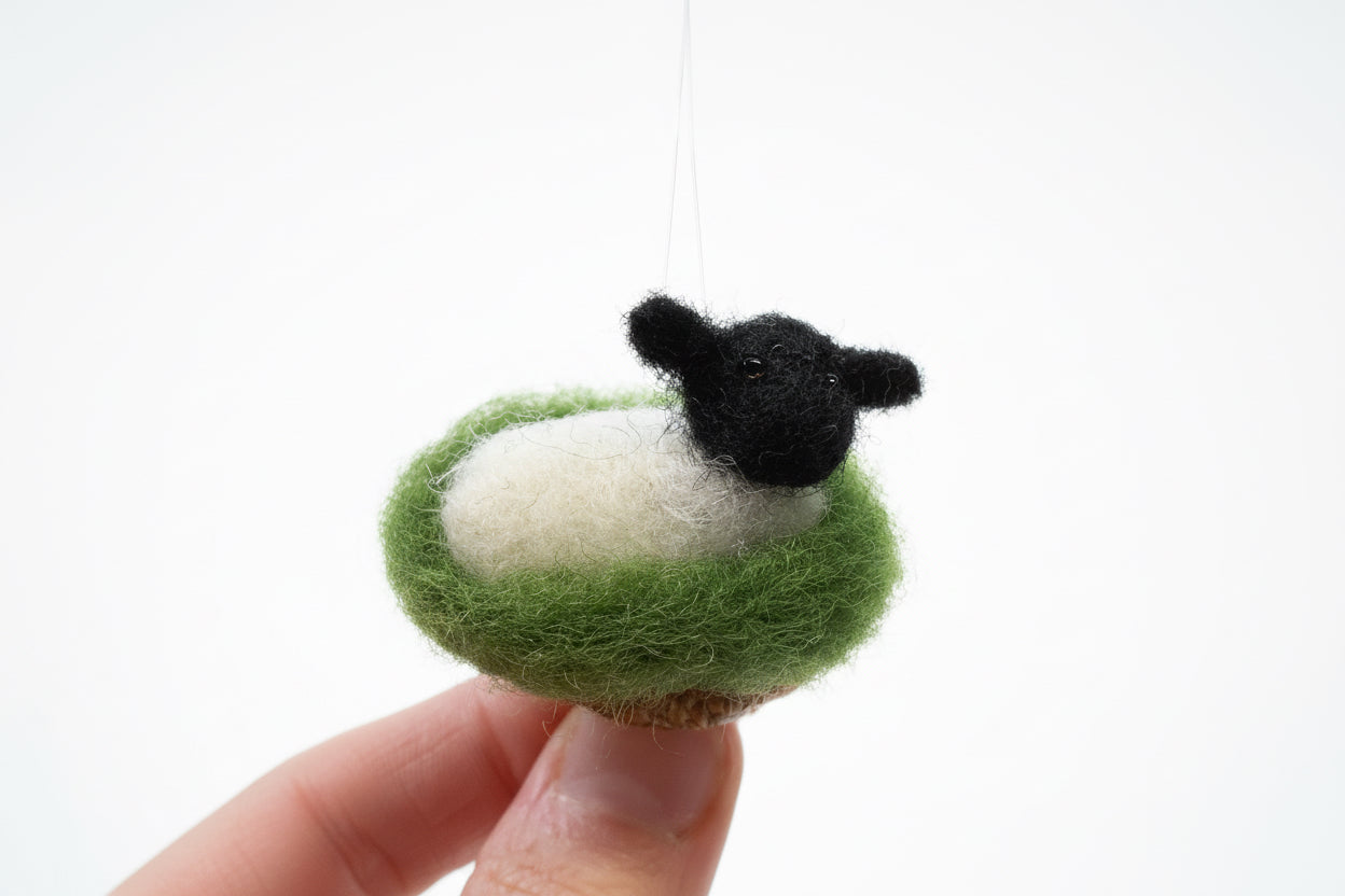 Handmade felt sheep ornament with a black face held against a white background