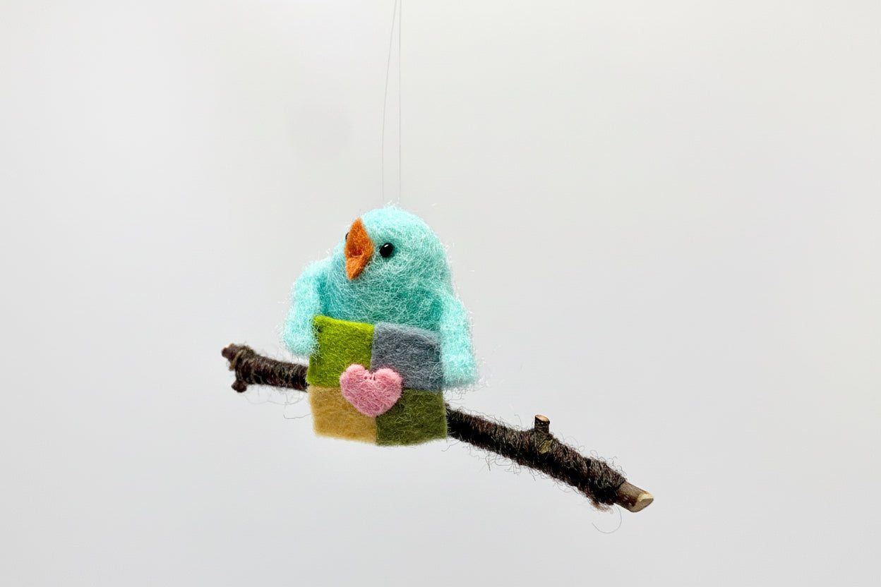 Felted bird ornament with a heart on a branch against a white background