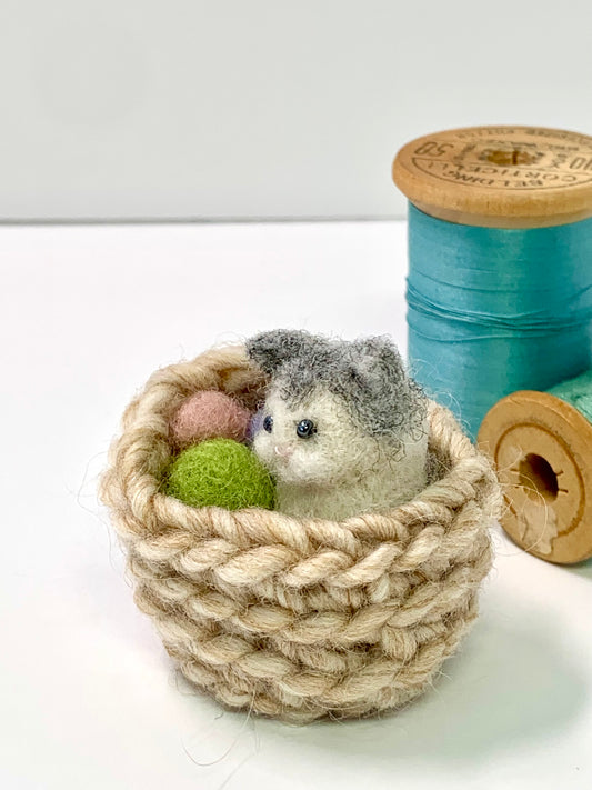 Small knitted basket with a toy cat and yarn balls on a white background
